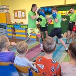 Dzieci siedzą na krzesełkach przed nimi dwie osoby boksują_ trzy obserwują.