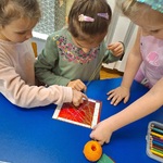 dziewczynki przy stoliku jedna trzyma nitkę_ dwie przyciskają ją do taśmy klejącej.