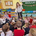 Nauczycielka zbliża się do dzieci wyciągając w ich stronę okładkę książki.