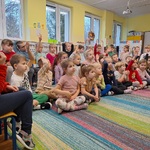 Dzieci siedza na dywanie_ kilkoro z nich podnosi rękę w górę