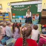 Dzieci siedzą na dywanie_ przed nimi na krześle siedzi nauczycielka SP5.