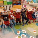grupa dzieci siedzi na krzesełakch i trzyma kartki z emblematem prezentu.