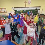 Dzieci stoją na dywanie i trzymają w górze worki z piłeczkami.