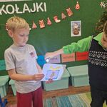 Jeden chłopiec trzyma kartkę z narysowanym prezentem_ a drugi chłopiec świeci na nią światłem z latarki.