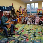 Dzieci siedząc patrzą na pana grającego na gitarze.