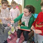 Grupa dzieci stoi wokół kobiety_ chłopiec otrzymuje naklejki.