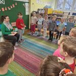 Dzieci stoją naprzeciwko kobiety i śpiewją piosenkę.