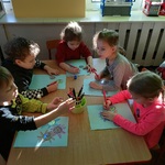 Dzieci siedzą przy stoliku i wykonują pracę plastyczną.
