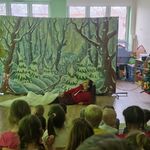 Kobieta leży na podłodze_ częściowo nakryta białą tkaniną_ w tle duża makieta przedstawiająca zimowy krajobraz.