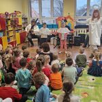 Dwoje dzieci stoi i naśladuje gesty kobiety w stroju anioła.