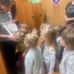 Dzieci będące w bibliotece słuchają opowiadania czytanego przez nauczycielkę.