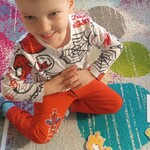 uśmiechnięty chłopiec siedzi obok kartki z pięcioma kropkami i sylwetą dinozaura z przyczepionymi spinaczami.