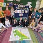 Dzieci prezentują dinozaura ułożonego z kolorowych karteczek na macie do kodowania.