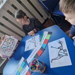 Chłopiec obserwuje Ozobota poruszającego się zgodnie z kodami_ a dziewczynka prezentuje swoją kartę dla robota.