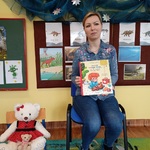 Kobieta siedzi na krześle i prezentuje książkę.