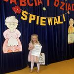 Dziewczynka z dyplomem stoi pod sceną.