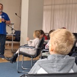 dzieci siedzą na krzesłach_ przed nimi stoi mężczyzna pokazuje tabliczki z ostrzegawcze.