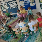 Pani siedzi na środku i czyta książkę_ dookoła siedzą dzieci na krzesełkach_