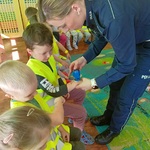 Pani policjantka stawia pieczątki dzieciom siedzącym na krzesełkach.