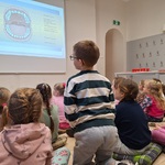 dzieci siedzą na poduszkach_ zwrócone w stronę ekranu.