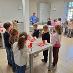 dzieci stoją przy stołach odwrócone w stronę prowadzącego.