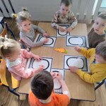 dzieci siedzą przy stoliku z kartkami_ na środku leży sylweta marchewki.