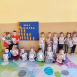 grupa dzieci ustawiona przy tablicy z sylwetami marchewek. Każde dziecko trzyma swoją kolorowankę.