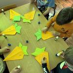 czworo dzieci układa marchewkę z origami na stole.