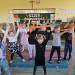 Dzieci stoją na dywanie_ w górze trzymają ręce z pomarańczowymi bibułkami.
