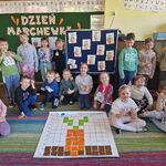 Dzieci pozują wokół maty_ na której jest ułożony obrazek marchewki.