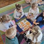 Grupa dzieci układa na dywaniku obrazki przedstawiające marchewki w różnych kombinacjach.