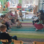  Dzieci siedzą na dywanie i słuchają bajki czytanej przez jedną z mam