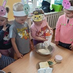 Przedszkolaki obserwują jak koleżanka wsypuje mąkę do miski.