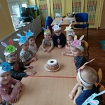 Grupa predszkolaków siedzi przy stolikach i patrzy na upieczoną babkę wielkanocną.