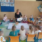 dzieci siedzą wokół białego materiału. Pani pokazuje wielkanocną serwetę.