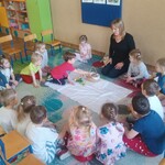 dzieci siedzą wokół białego materiału_ chłopiec wkłada jajko do koszyczka.