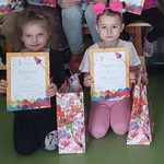 Dwie dziewczynki trzymają w rękach dyplom ,obok stoją w torebkach nagrody.