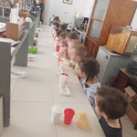 Dzieci stoją wzdłuż stołu na którym ustawione są rzeczy potrzebne do odlewu 