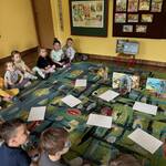 kilkoro dzieci siedzi na dywanie dookoła rozłożonych książek.