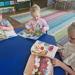 Trzy dziewczynki siedzą przy stole i oglądają książki.