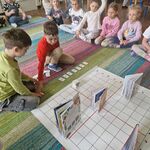 Dwóch chłopców siedzi obok maty do kodowania i układają program dla Genibota.