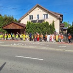 Dzieci w kolorowych kamizelkach idą parami chodnikiem przy ulicy.