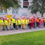 dwie najstarsze grupy stoją na chodniku przed przedszkolem w ręku trzymają chorągiewki.