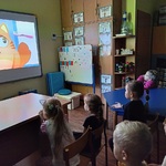 Dzieci siedząc na krzesełkach oglądają film edukacyjny.