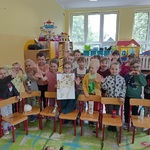 Grupa dzieci stoi za krzesełkami _ na których leżą przybory do higieny osobistej.