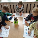 Przedszkolaki kolorują przy stoliku karty pracy.