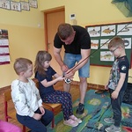 Dwoje dzieci oglada wędkę pokazywaną przez wędkarza.