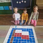 Troje dzieci pozuje przy macie do kodowania_ na której z kartoników ułożona jest flaga Polski.