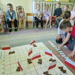 Dzieci siedzą na krzesełkach_ a dwoje dzieci jest naśrodku dywanu i zaprogramowuje Genibota.