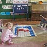 Na dywanie leży mata do kodowania_ dziewczynka układa na niej kolorowe kartoniki.
